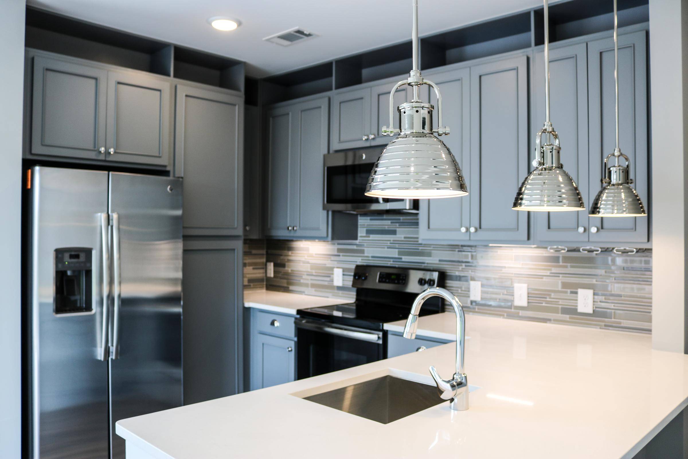Modern kitchen with gray cabinets, stainless steel appliances, pendant lights, and a white island sink at Carolina Square apartments
