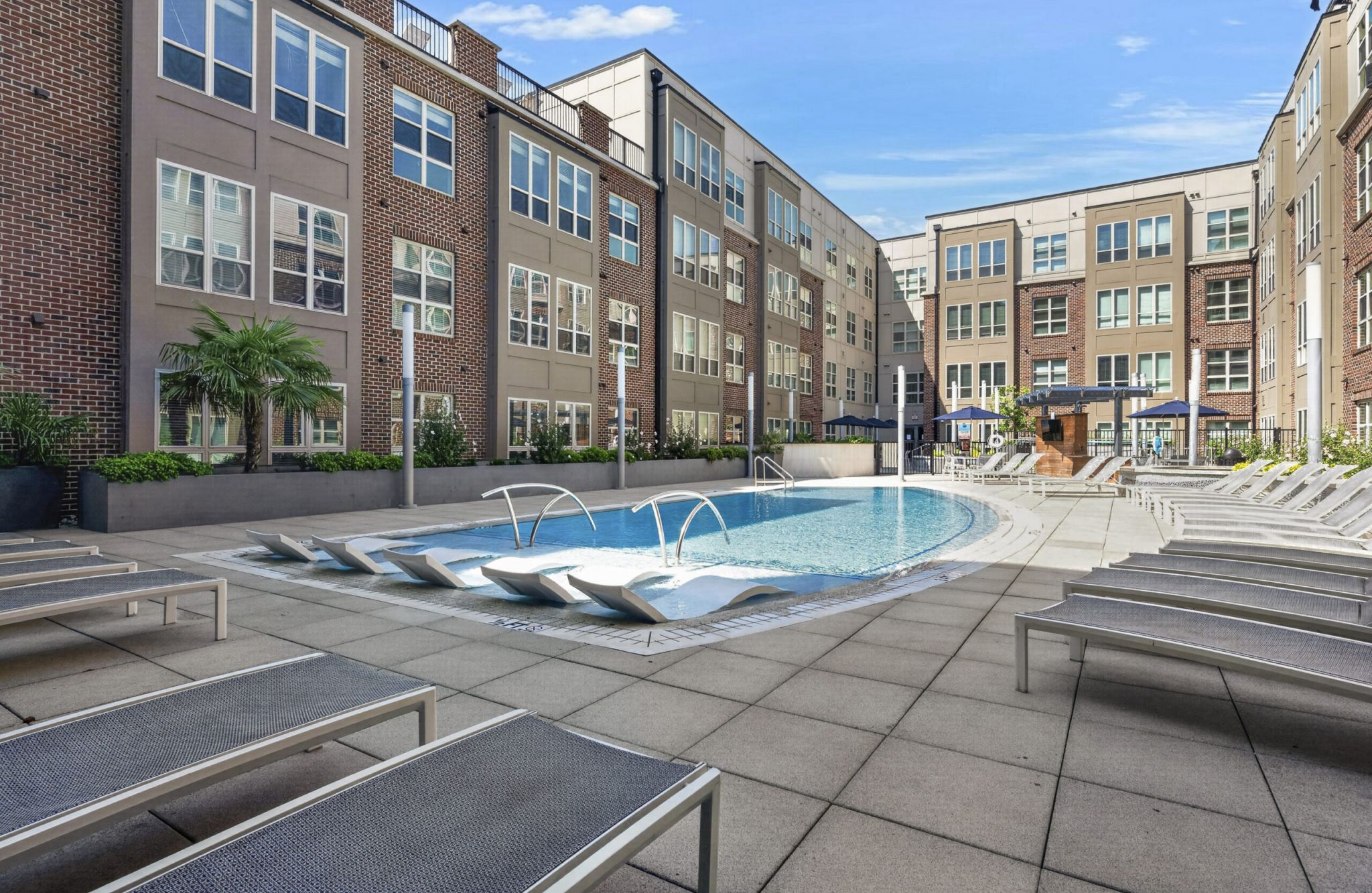 Outdoor pool area with lounge chairs, surrounded by modern apartment buildings under a clear blue sky.