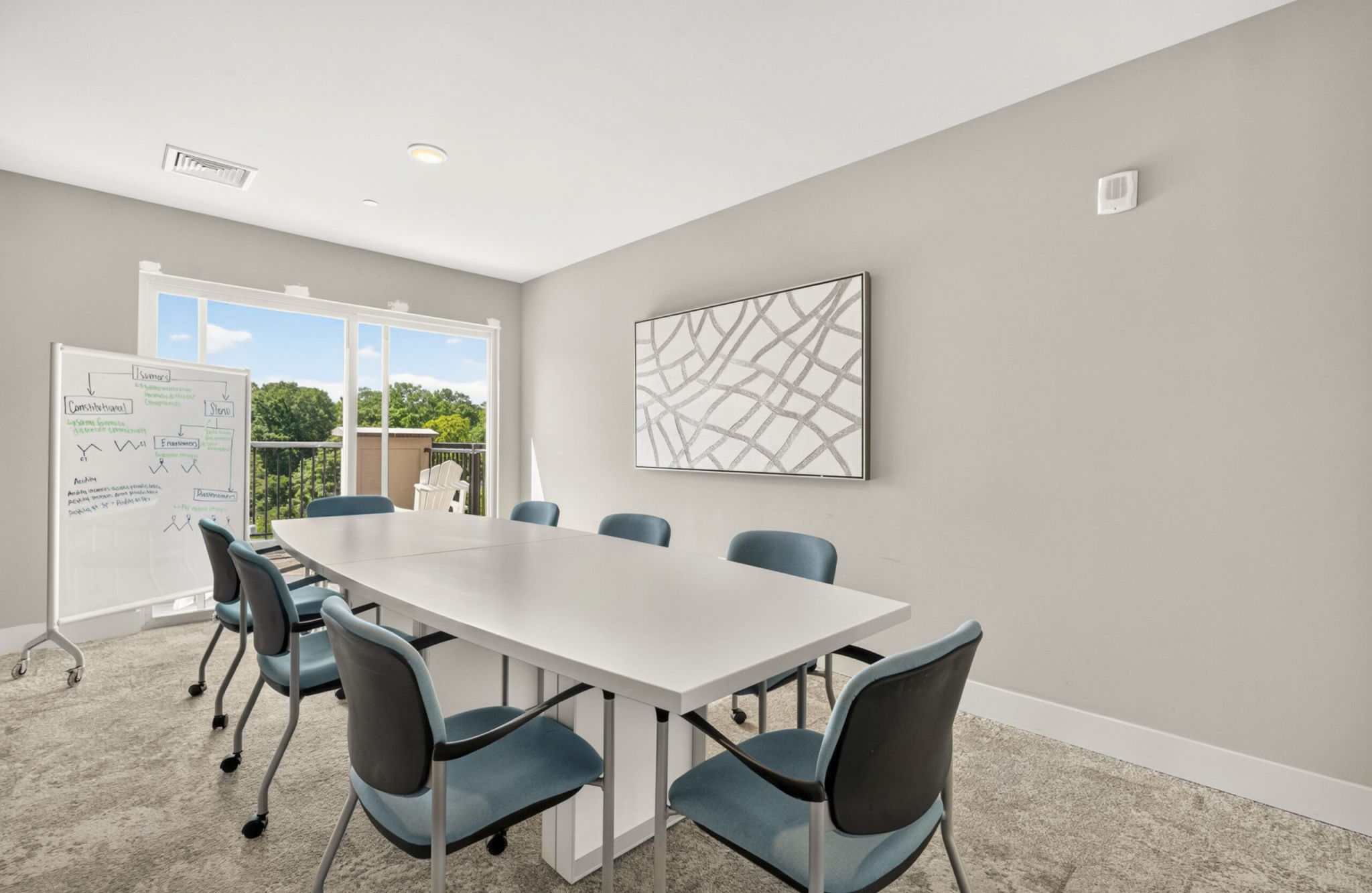 Modern conference room with six blue chairs, white rectangular table, whiteboard, large window, and abstract wall art.