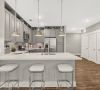 Modern kitchen with gray cabinets, stainless steel appliances, island with sink, and three clear stools on wood flooring.