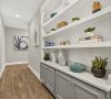 A hallway with wood floors, built-in white shelves displaying vases, plants, and decor, and abstract art on the wall at the end.