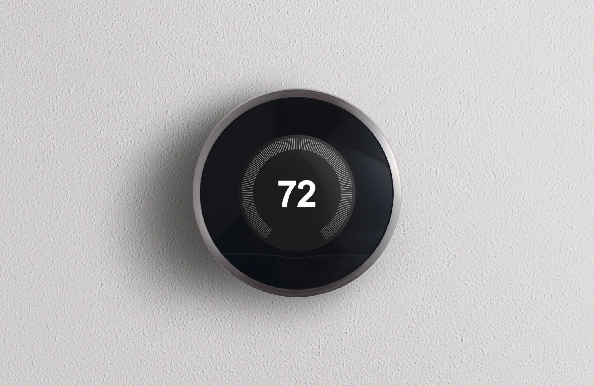 A round digital thermostat displays the temperature set to 72 degrees on a white textured wall.